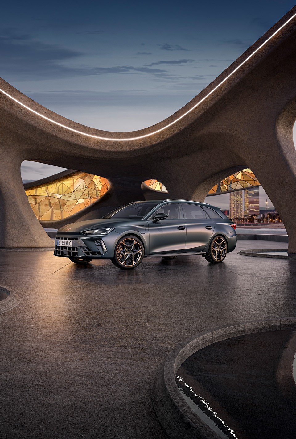 A wide-angle view of the sporty new CUPRA Leon Sportstourer 2024 hybrid vehicle in a matte grey, parked in an urban setting, in front of large gaudi-inspired geometric windows.
