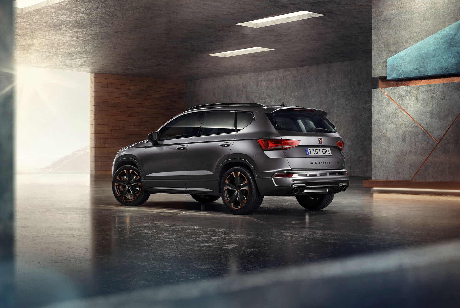 Pilkas „CUPRA Ateca“ SUV baltame fone. Automobilis su tvirtomis priekinėmis grotelėmis, LED priekiniais žibintais ir lengvojo lydinio ratlankiais su vario akcentais, pabrėžiančiai sportišką automobilio išvaizdą.