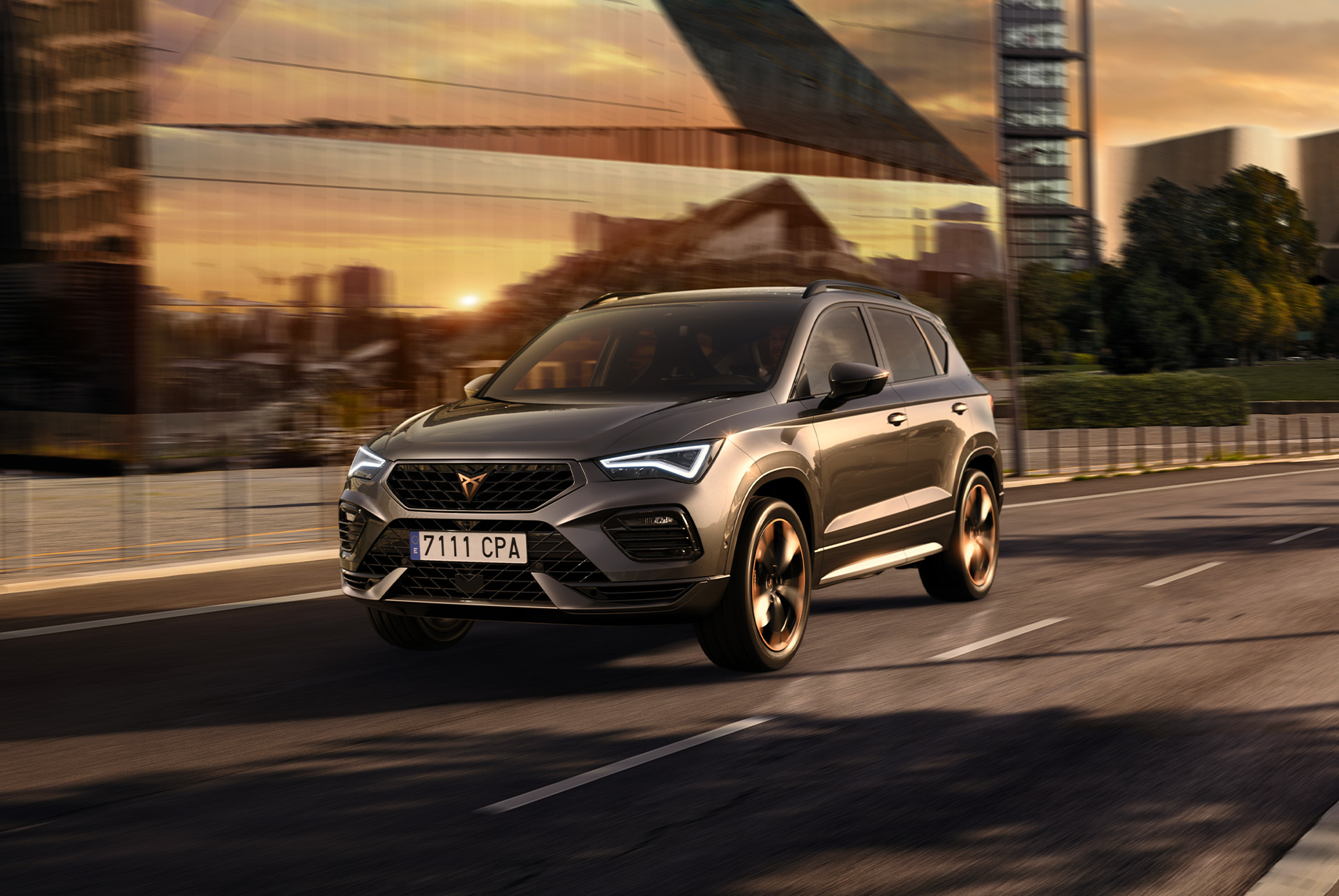 Pilkas „CUPRA Ateca“ SUV baltame fone. Automobilis su tvirtomis priekinėmis grotelėmis, LED priekiniais žibintais ir lengvojo lydinio ratlankiais su vario akcentais, pabrėžiančiais sportišką automobilio išvaizdą.