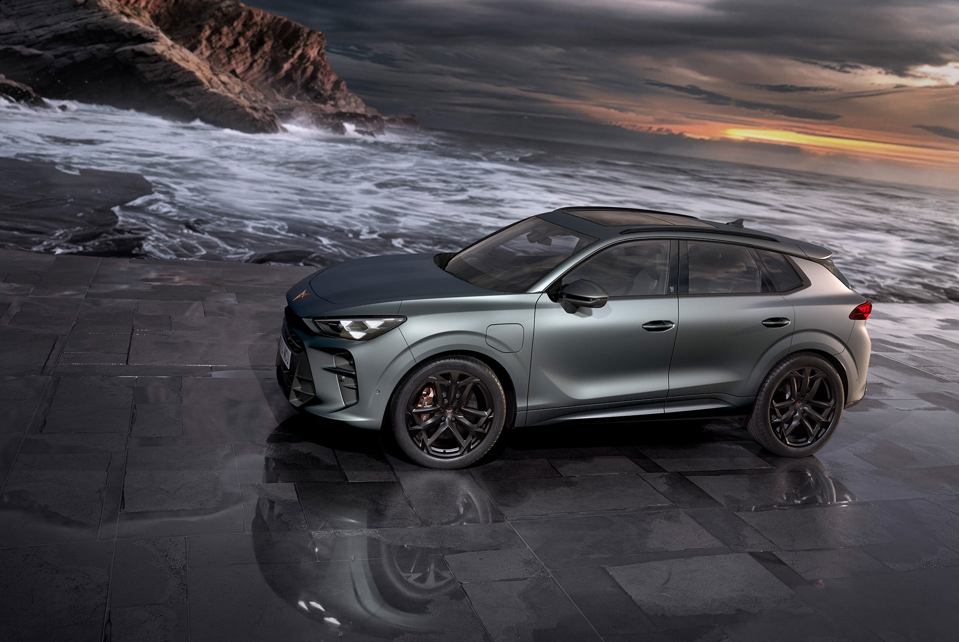 cupra terramar hibridinis SUV, naujas modelis, vaizdas iš šono, su 20 colių america’s cup lengvojo lydinio ratlankiais ir akebono stabdžiais, pilka matinė enceladus grey matt spalva, ant šlapio grindinio prie jūros, saulėlydis. 